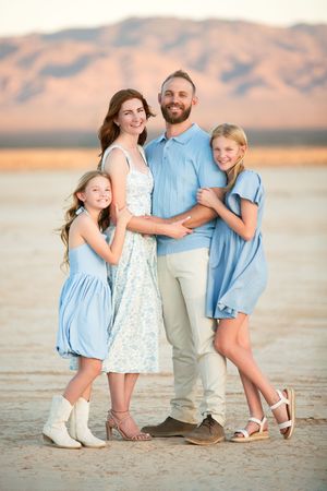 Family of four posing in desert landscape, parents and two girls in coordinating blue outfits with mountain backdrop.