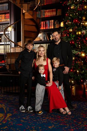 Family of five posing in front of a decorated Christmas tree in an elegant library setting with bookshelves.