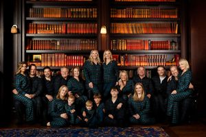 Large family group portrait in matching plaid pajamas posing in front of a dark wood bookshelf filled with books.
