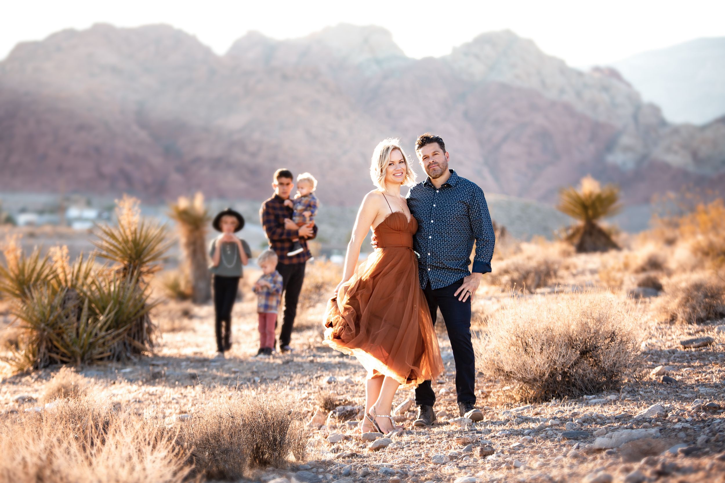 Group walking through desert landscape with red rock formations in background.