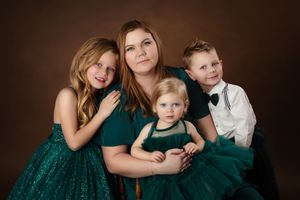 A mother poses with her three children in matching emerald green outfits against a warm brown studio backdrop.