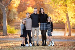 Family of five poses together during autumn in a park with golden foliage.