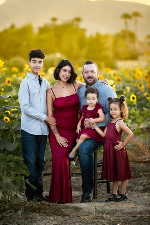 Family of five posing in a sunflower field at golden hour, wearing coordinated red and blue outfits.