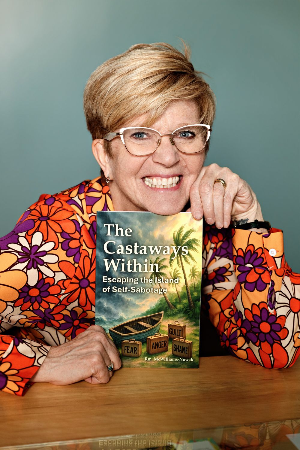 Woman smiling and holding 'The Castaways Within: Escaping the Islands of Self-Sabotage' book.
