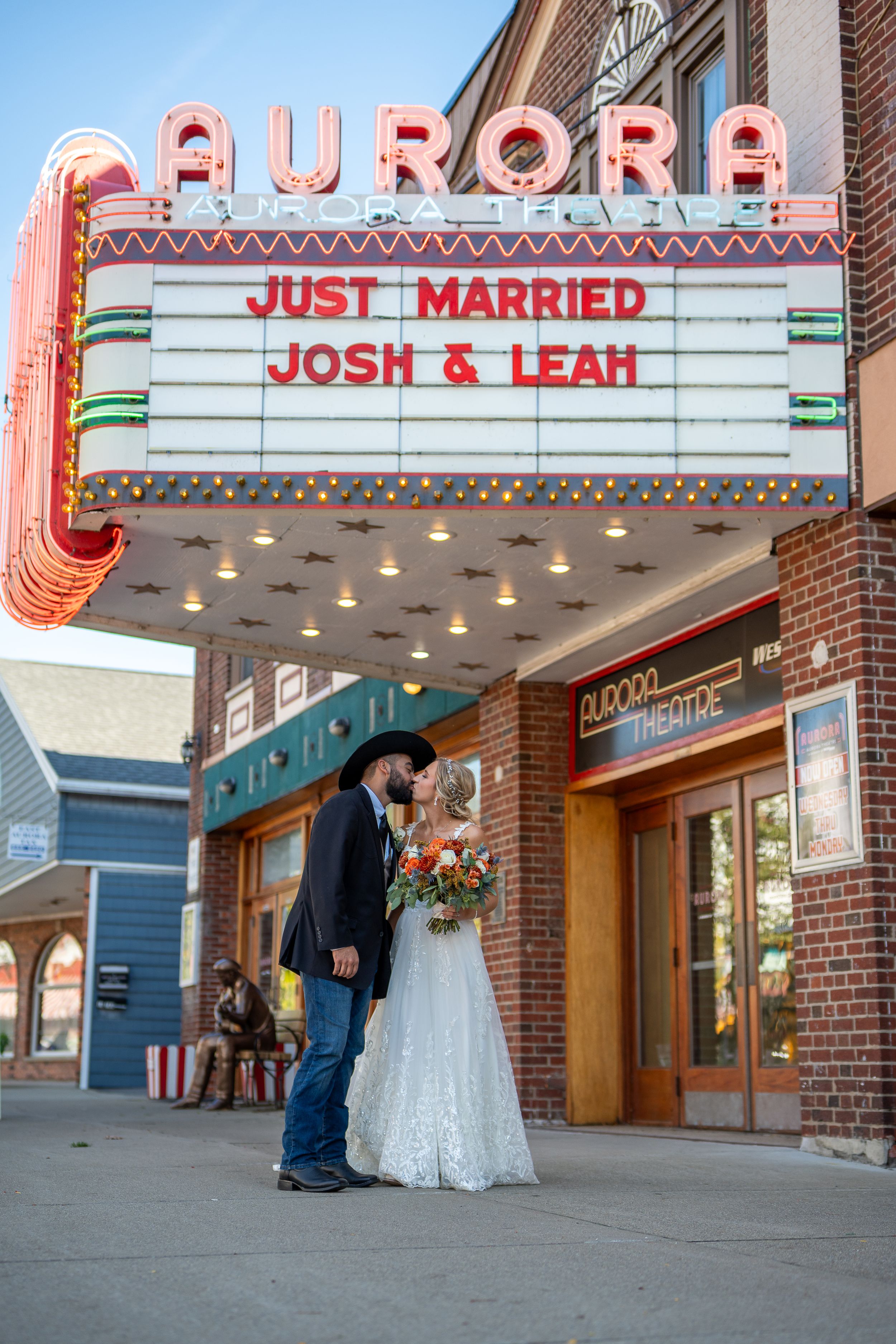 Newlyweds pose beneath vintage Aurora theater marquee displaying Just Married message.