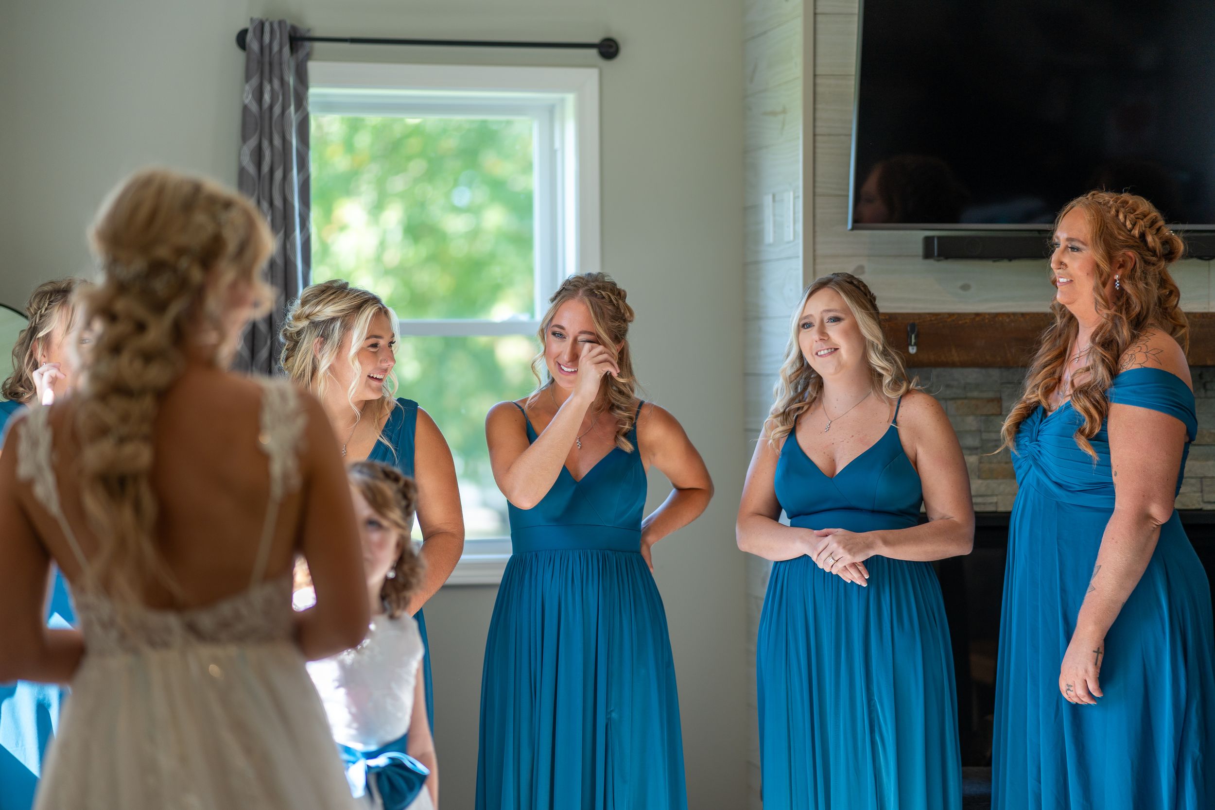 Bridesmaids in matching blue dresses react emotionally to seeing the bride.