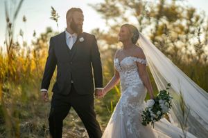 Newlyweds share a romantic moment in golden hour light among tall grass.