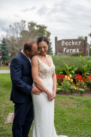 Romantic couple embracing in front of Becker Farms sign surrounded by colorful garden flowers.