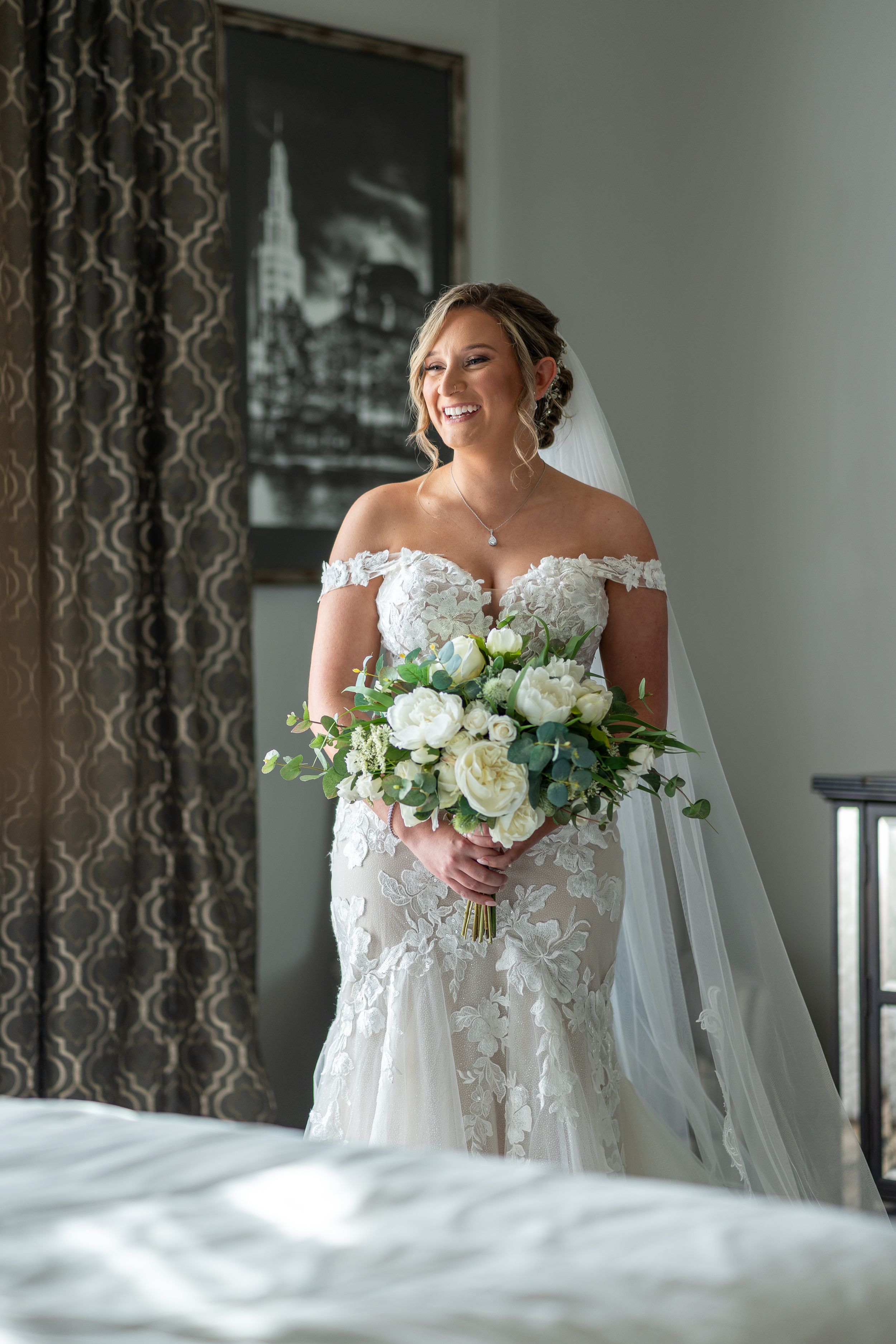 A bridal portrait showing intricate lace dress details and white rose bouquet near a window.