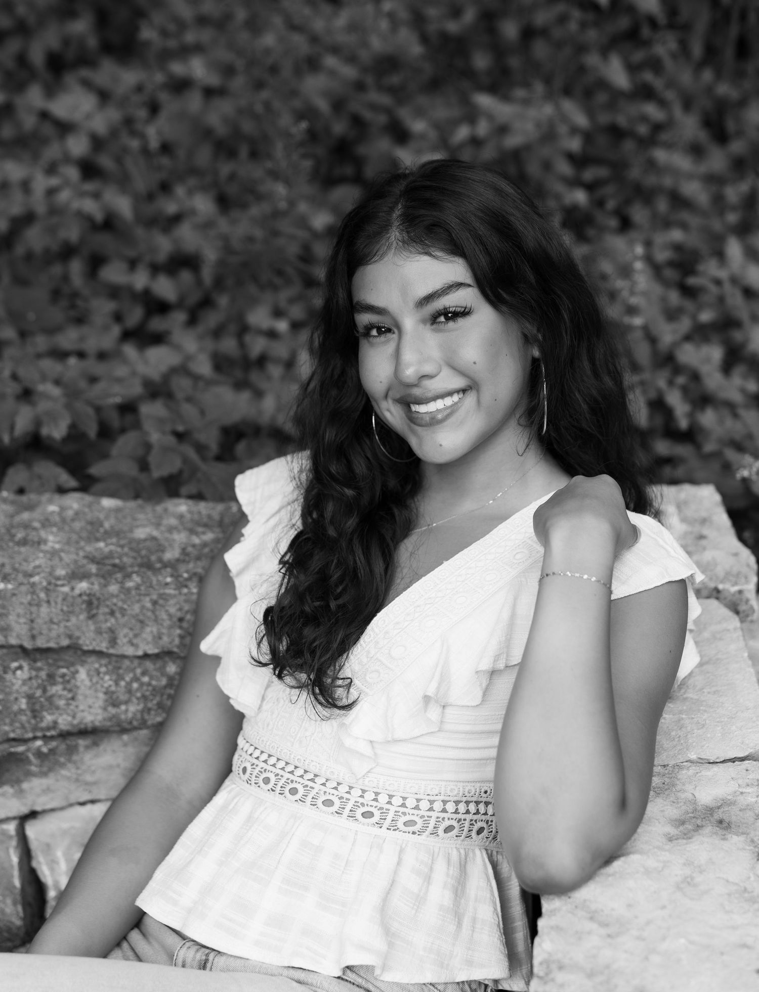 A person in a white ruffled dress poses against a stone wall in a black and white photograph.