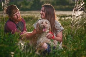 A man and a woman with a dog in a field of grass.