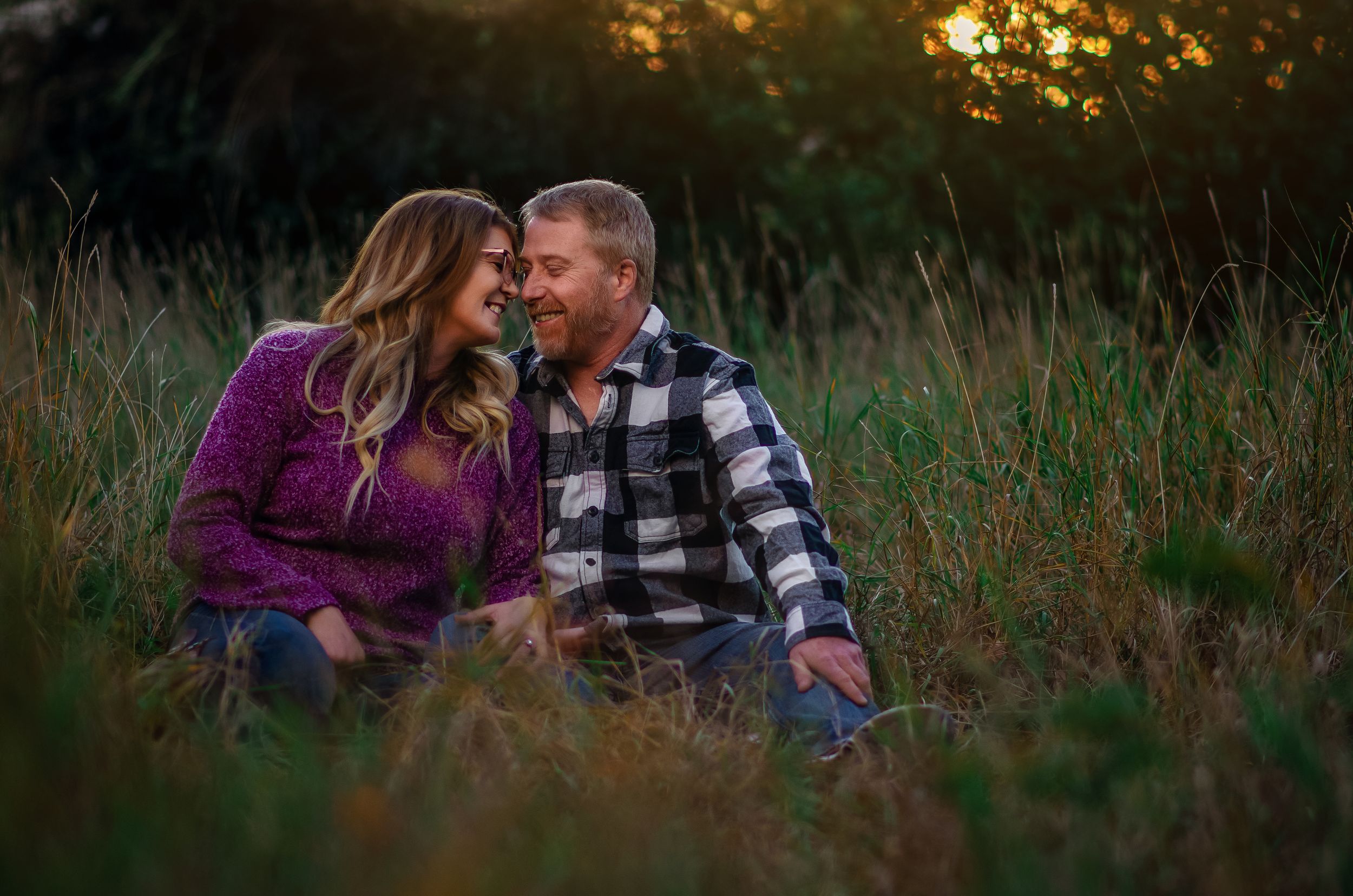 A man and a woman sitting closely together in a field of grass.