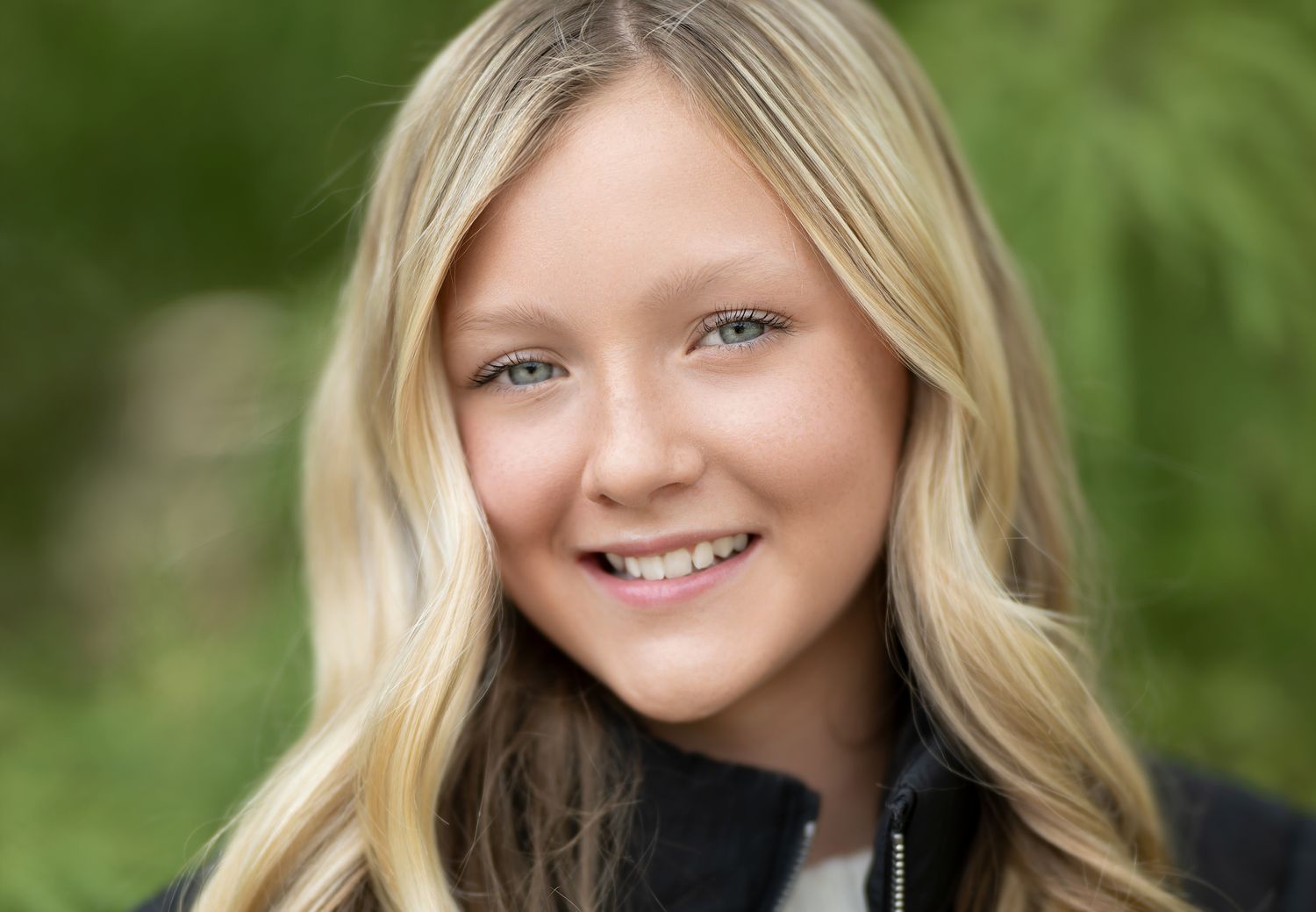 Professional outdoor portrait with soft natural lighting and green foliage background.