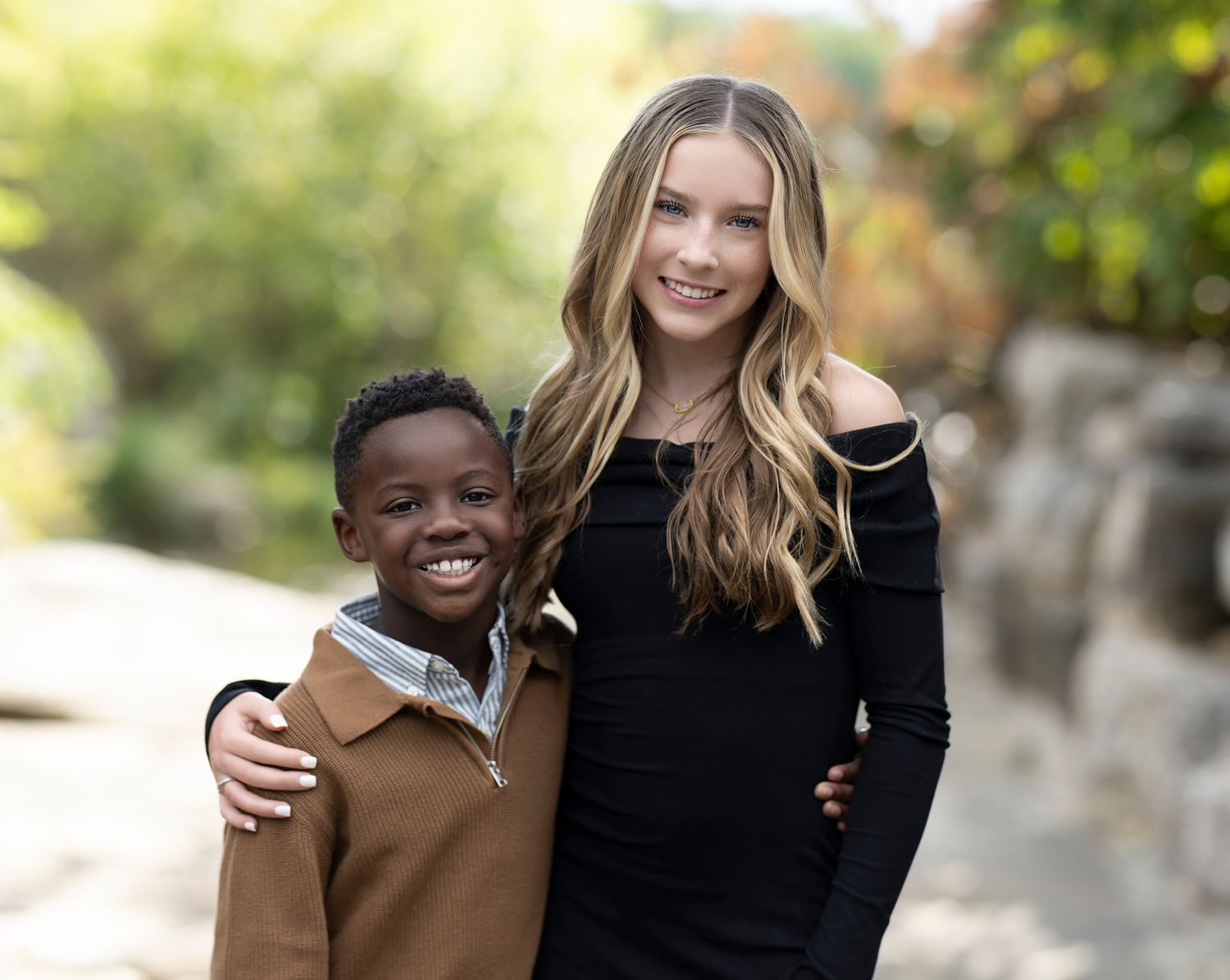 Heartwarming outdoor portrait of two siblings embracing and smiling together.