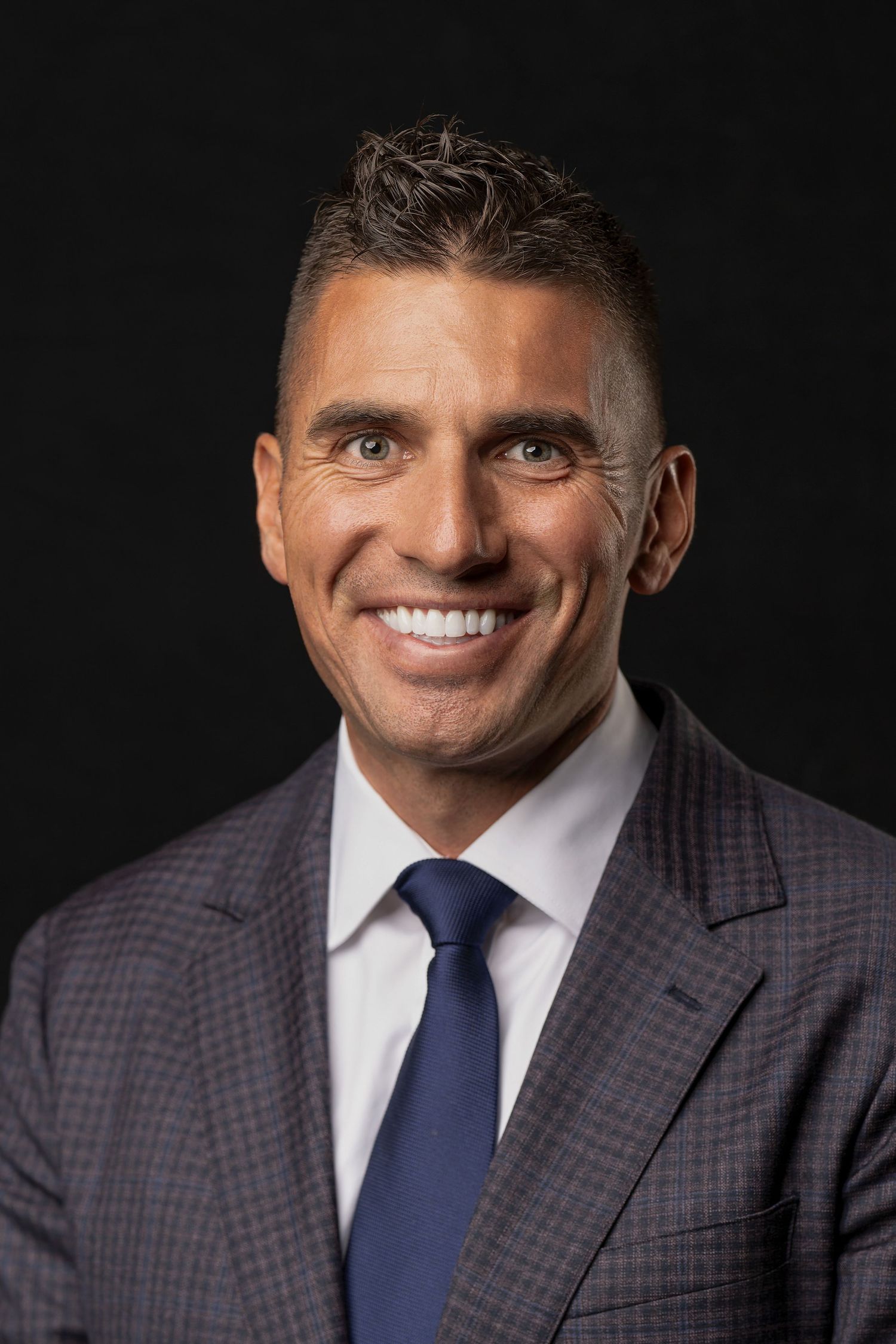 Professional business headshot of person in checkered suit with navy tie.