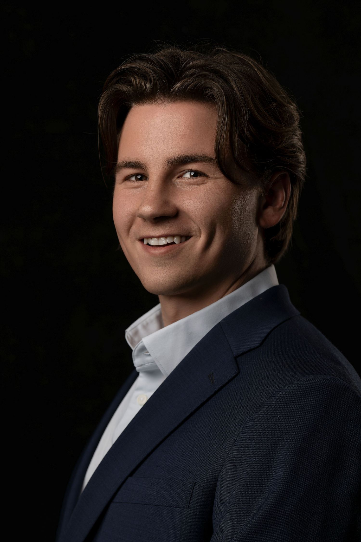 Professional headshot of person in business attire against dark background.