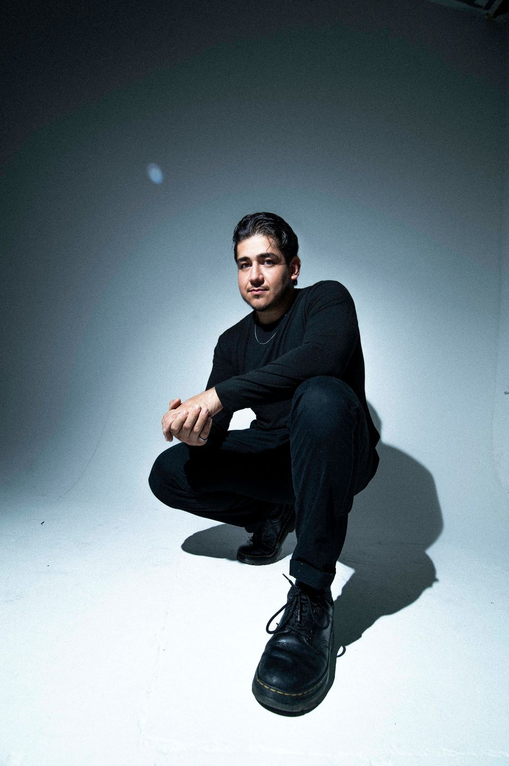 A person in black clothing crouches against a light gray background in an artistic photo series.