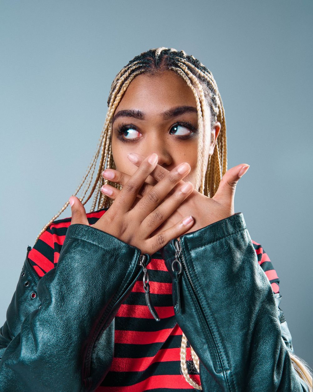 Playful fashion portrait with striped shirt and denim jacket against blue studio background.