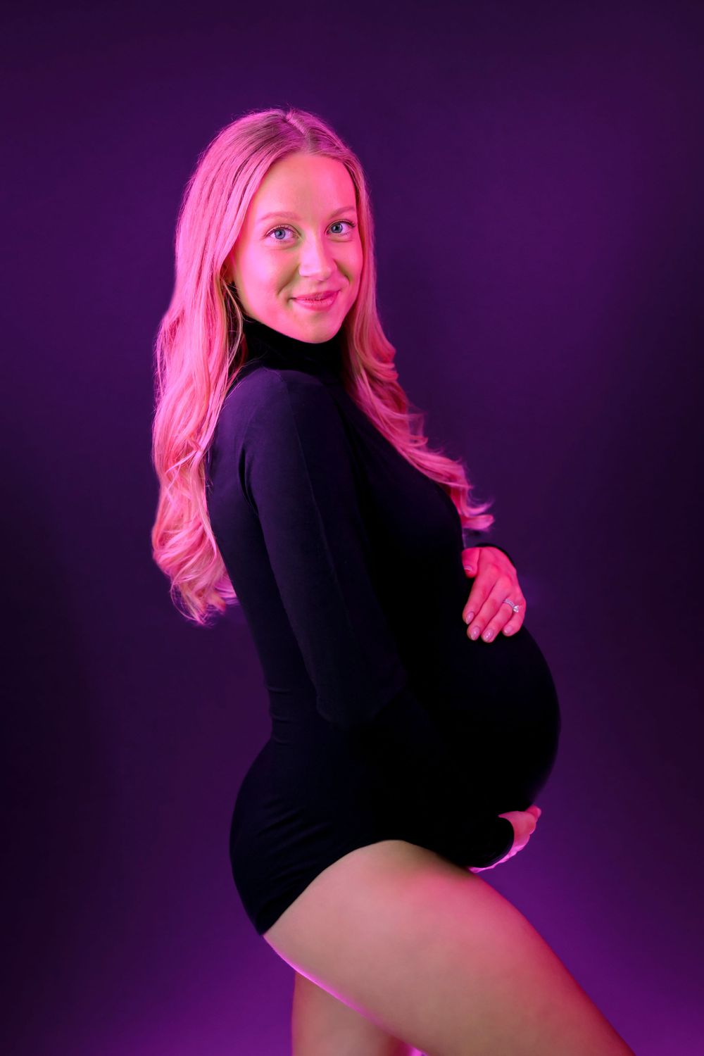 mom holding baby bump in black outfit and pink lights