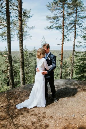 Brudepar står tett mot hverandre blant høye trestammer og på en liten topp med utsikt.