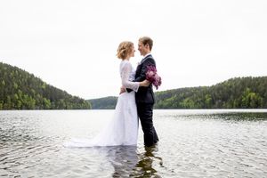Brudepar tett inntil hverandre mens de står i vannet. Omringet av vann og skog.