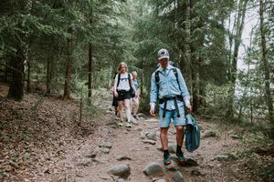 Brudgom gående fornt nedover steinete sti i skogen. Han har på seg turklær og bærer dressen i dresspose i hånden.