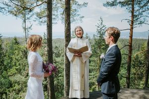 Brudepar og prest under ekteskapsinngåelsen. Presten ser i kamera og brudeparet ser på presten.