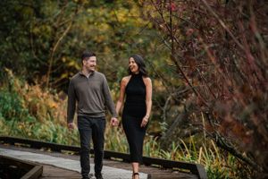 Couple walking on wooden boardwalk surrounded by autumn foliage.