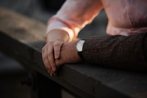 Two people holding hands on a wooden bench, one wearing a white watch, in a tender romantic moment.