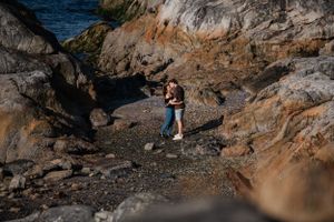 Couple embracing on rocky coastal path with ocean cliffs in background.