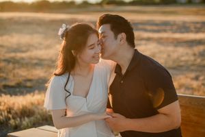 A romantic couple embraces during golden hour in a field, bathed in warm sunlight.