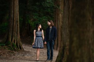 Two people walking on a forest path between tall trees wearing casual elegant clothing.