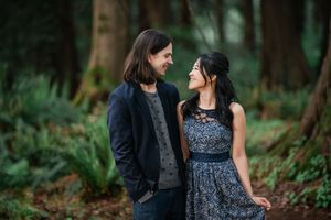 A couple shares a loving gaze while standing in a misty forest setting, wearing casual stylish outfits.