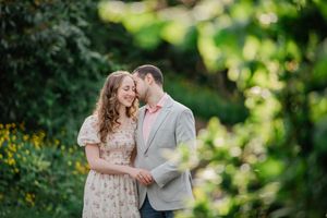 Couple shares tender moment together in garden setting with yellow wildflowers and green foliage in background.