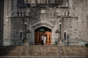 A couple stands in the grand stone entrance doorway of a historic Gothic church building with stone steps.