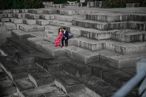 Two people sit together on stone steps in a dramatic black and white photo with a pop of bright pink color.