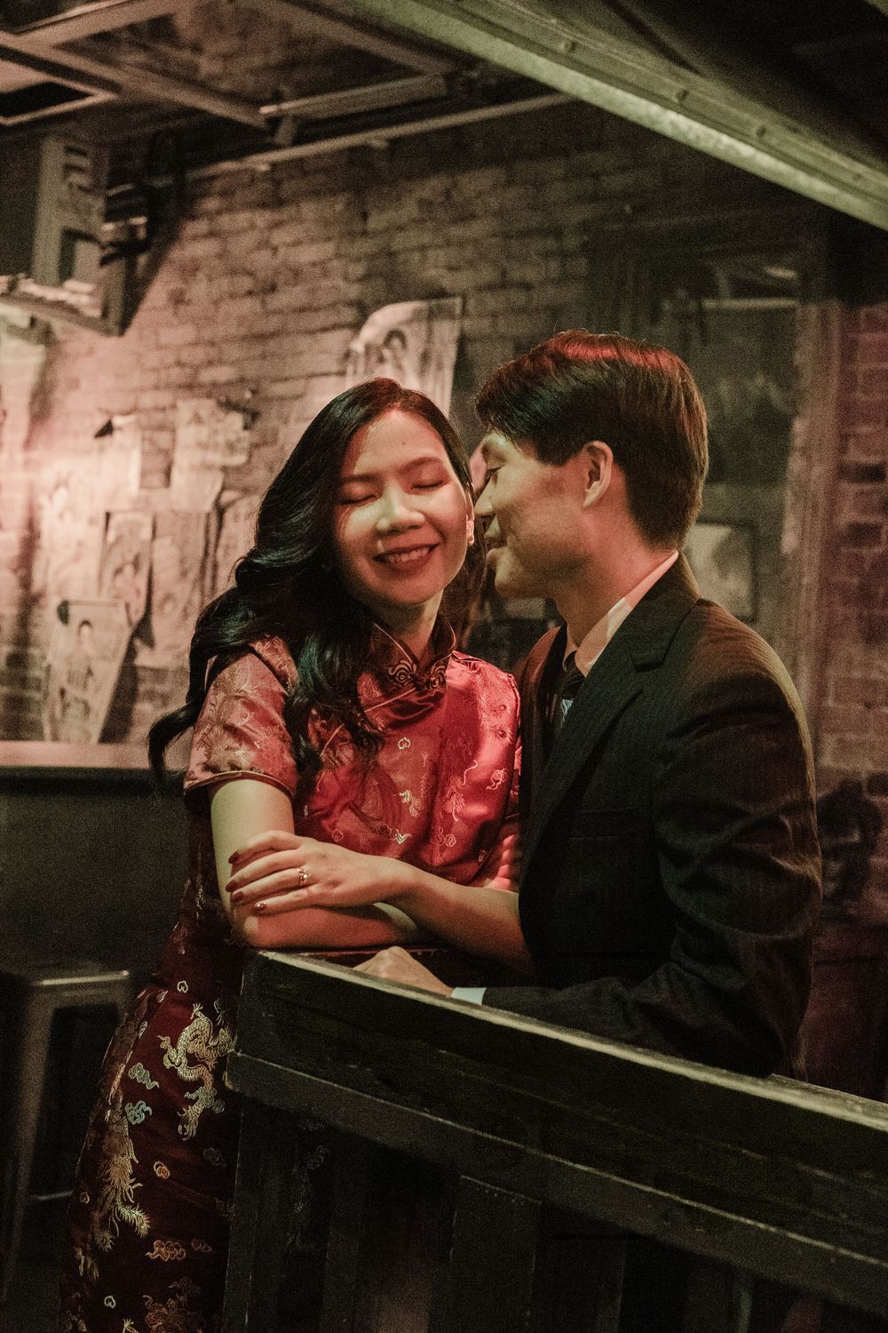 Couple in vintage attire sharing a romantic moment on a balcony, woman in red qipao smiling joyfully.