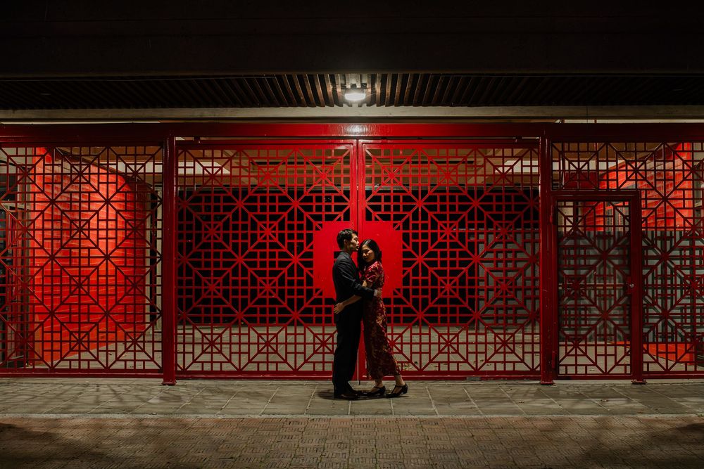 Couple embracing in front of illuminated red decorative panels at night, creating a romantic and vibrant backdrop.