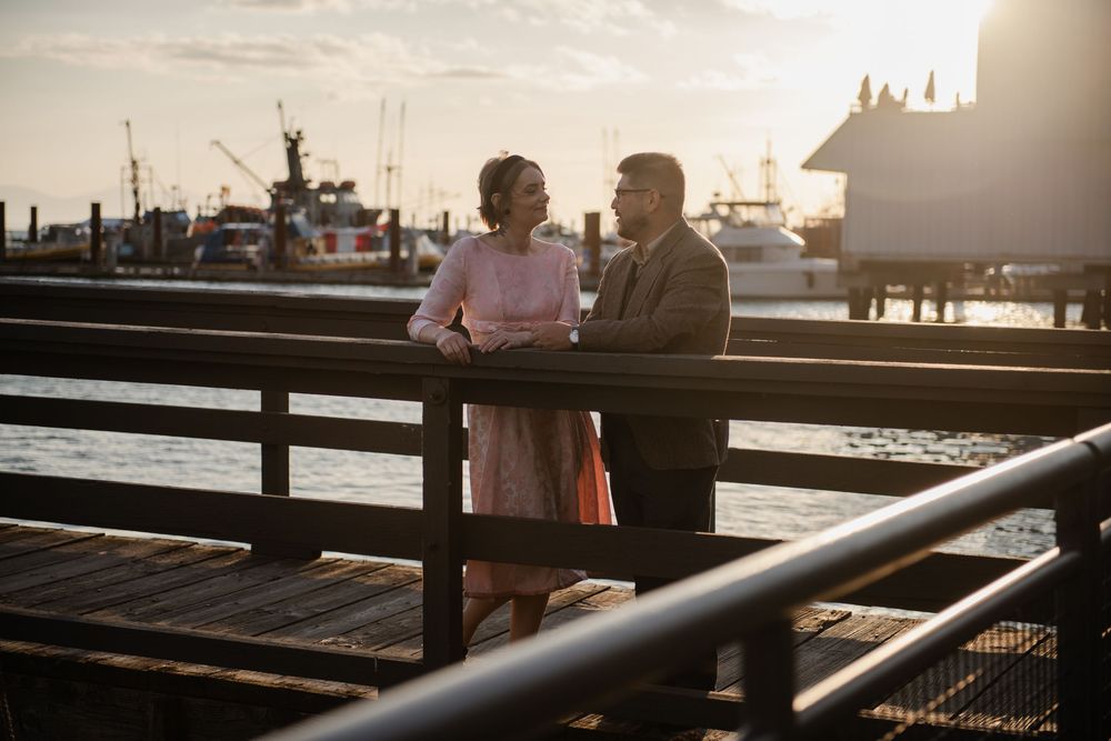 Couple in vintage attire sharing a romantic moment on a waterfront dock at golden hour sunset.