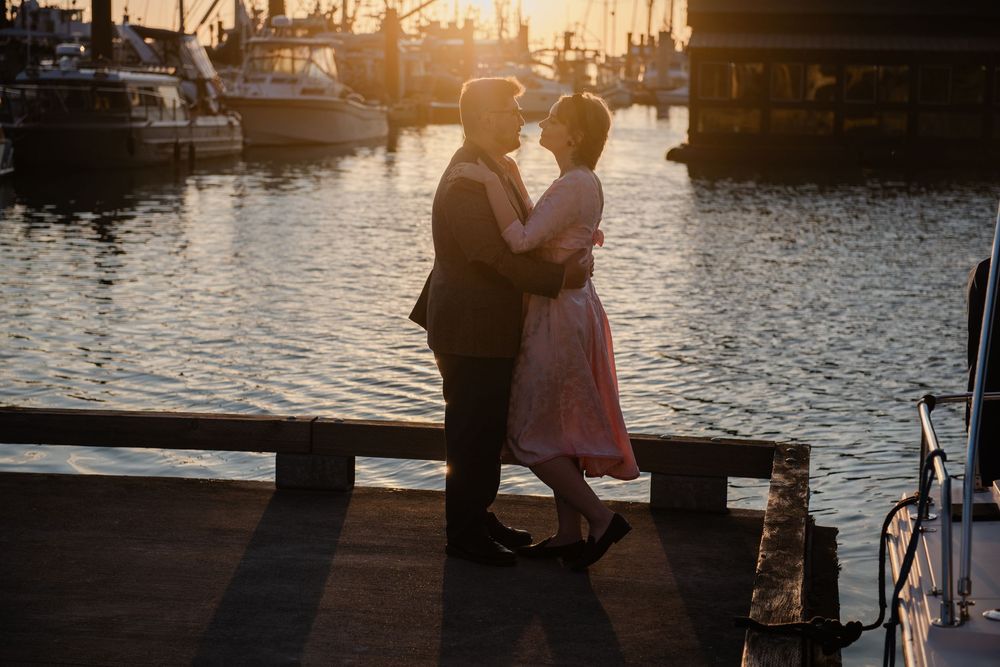 Couple embracing at sunset on a marina dock, golden light reflecting on the water with boats in the background.