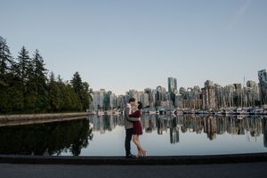 A scenic view of Vancouver's downtown skyline reflecting in calm waters at Stanley Park Seawall during sunset.