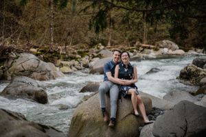 A couple sits together on rocky outcroppings beside a rushing mountain stream.