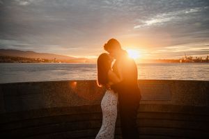 Silhouetted figures embrace against a golden sunset over the water.
