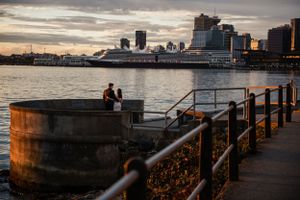A romantic moment at the harbor with a cruise ship and city skyline in the background.