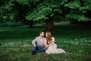 A couple sits together on a lush green lawn dotted with small white wildflowers in a peaceful garden setting.