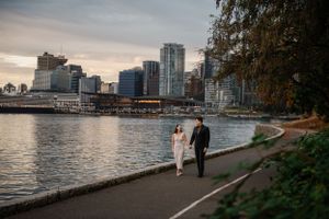 A couple walks along the seawall with Vancouver's modern skyline in the background.