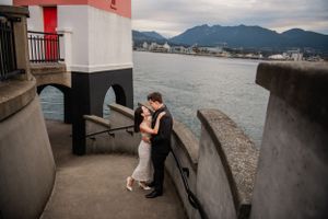 A couple shares an intimate moment by the lighthouse with mountains in the distance.