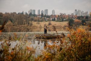 Silhouetted couple on dock with city skyline in distance during fall season.