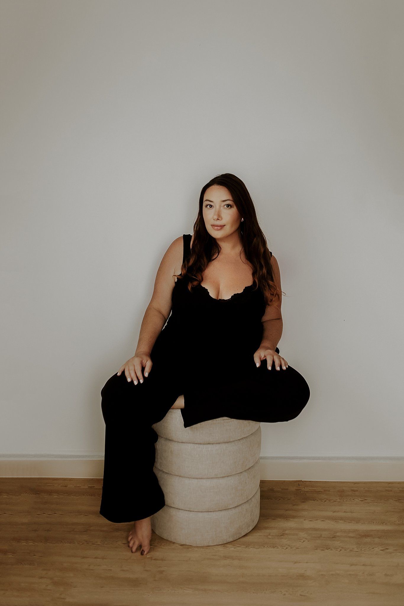 Artistic portrait series showing a person in black against neutral backdrop with round ottoman.