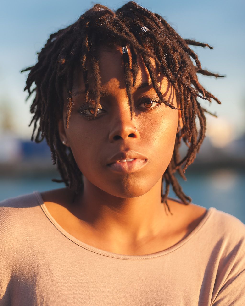 Portrait shot in golden hour light showing dreadlocks silhouetted against a blurred background.